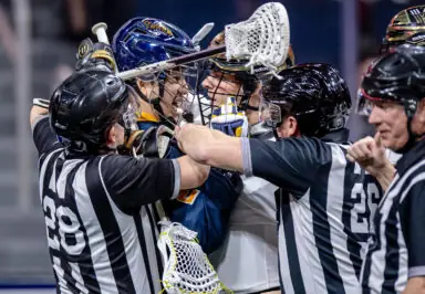 A confrontation between players in a lacrosse game, with referees intervening to separate them.