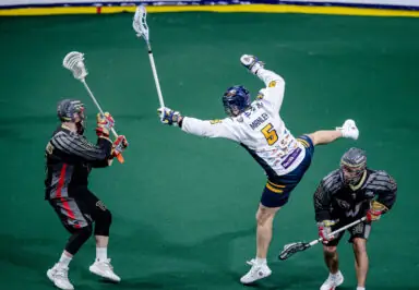 A player in a white jersey attempts a shot while another player in black defends, with a third player nearby.