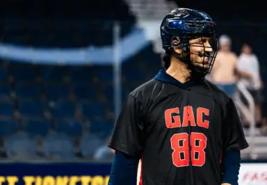 Lacrosse player wearing a black jersey with "GAC 88" smiles during a game.
