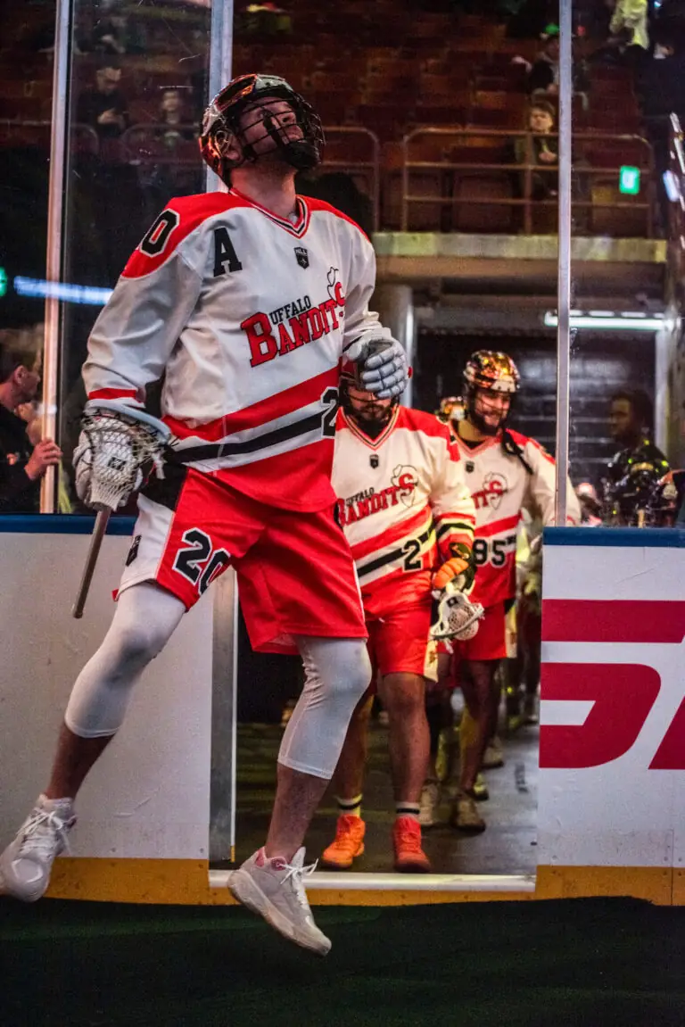 Buffalo Bandits players entering the arena, wearing red and white uniforms, with one player in the forefront celebrating.