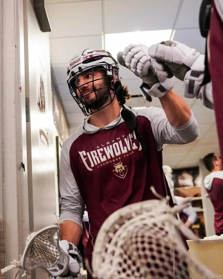 Lacrosse player in Albany FireWolves gear greeting teammates in a locker room.