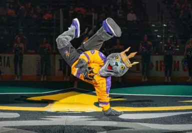 A costumed mascot with a gray wolf head and crown breakdancing on the lacrosse field.