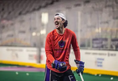 A lacrosse player in a red shirt with the "Panther City" logo celebrates on the field, holding a stick and looking excited.