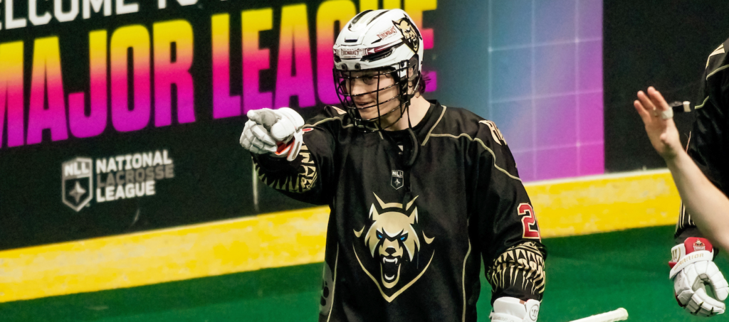 Lacrosse player in a black jersey points while celebrating on the field during a National Lacrosse League game.