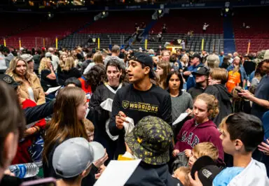 A crowd of fans gathers around a Vancouver Warriors player, who is signing autographs at a lacrosse event.