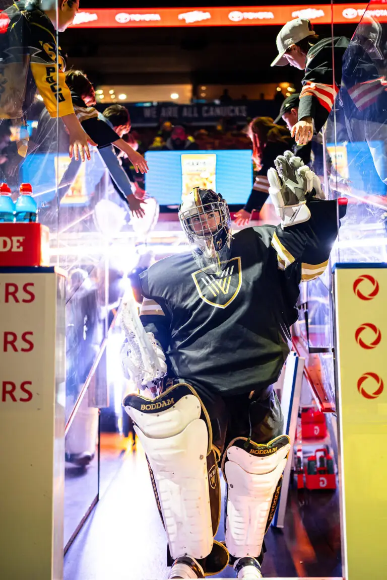 A lacrosse goalie in black and white gear waves to fans as they exit the tunnel onto the field.