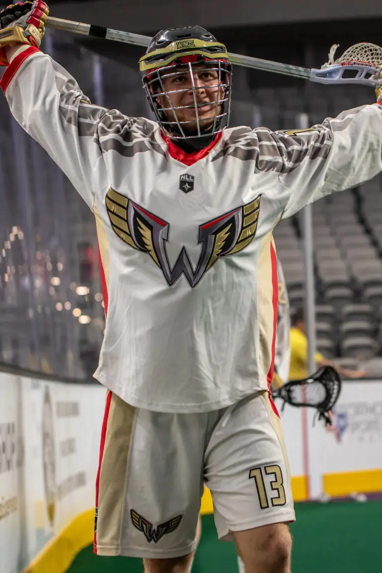 Lacrosse player celebrating, wearing a white jersey with a bold logo, number 13, and a helmet.