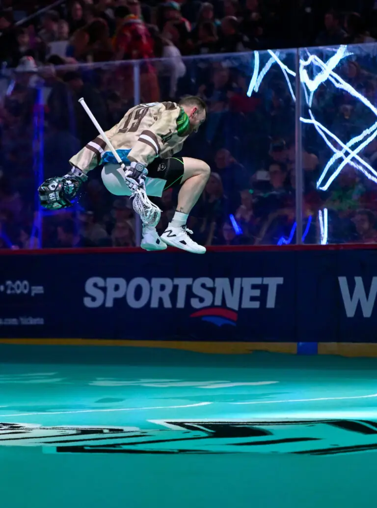 A lacrosse player leaps mid-air while holding his stick above a brightly colored turf during a game.