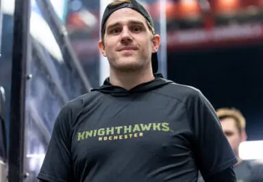 A man in a black hoodie with "KNIGHTHAWKS ROCHESTER" printed on it, standing near the team