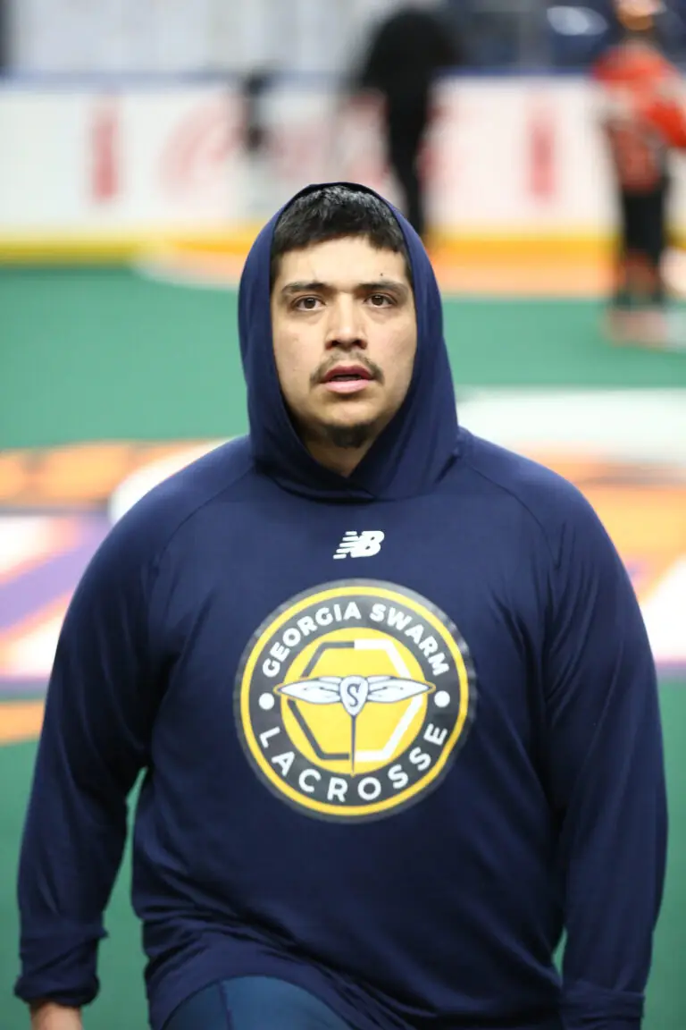 A lacrosse player wearing a navy hoodie with the Georgia Swarm logo, walking on a green field.