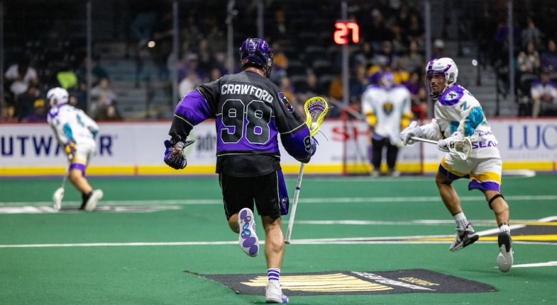 Lacrosse players in action on the field, one wearing a black jersey with "CRAWFORD" and the number 98, while another in a white jersey defends.
