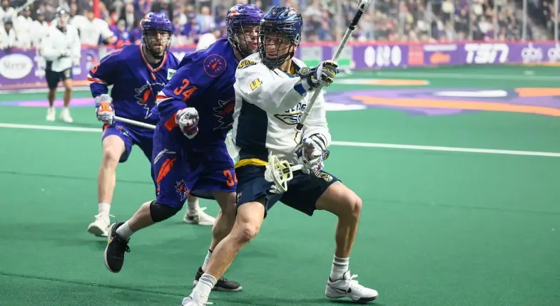 A lacrosse player in a white jersey prepares to shoot while being defended by another player in a blue jersey.