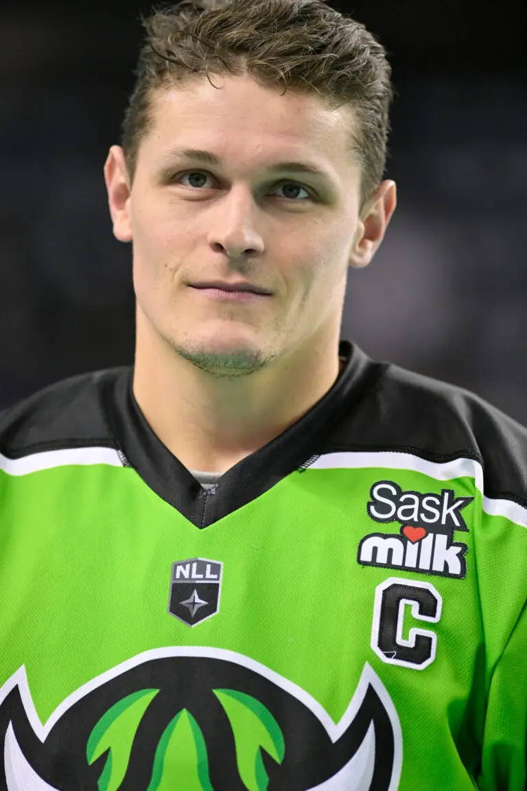A lacrosse player in a green jersey with black accents, featuring the NLL logo and the captain