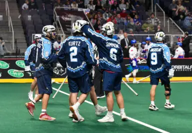 Lacrosse players in blue jerseys celebrate on the field during a National Lacrosse League game.