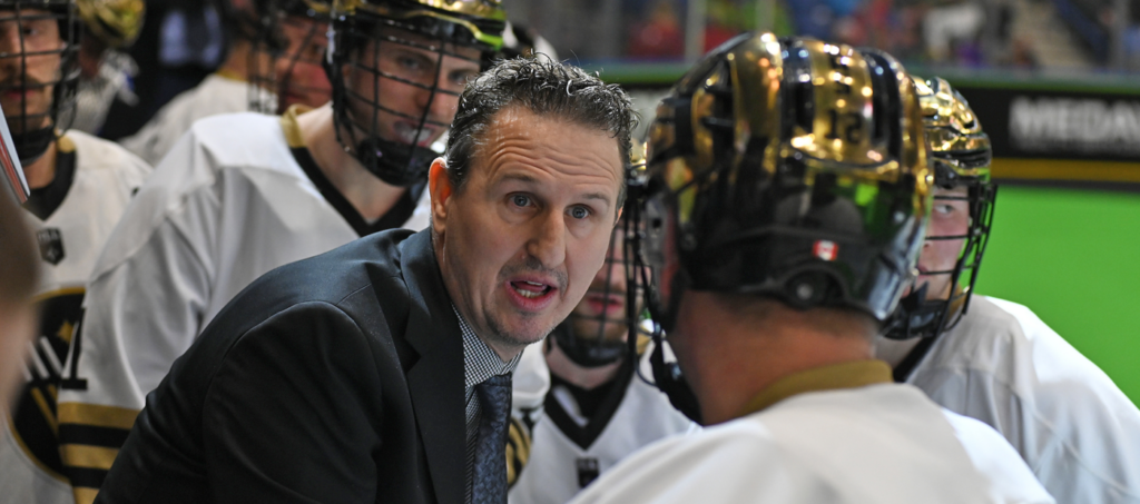A coach speaks to players in a huddle during a lacrosse game.