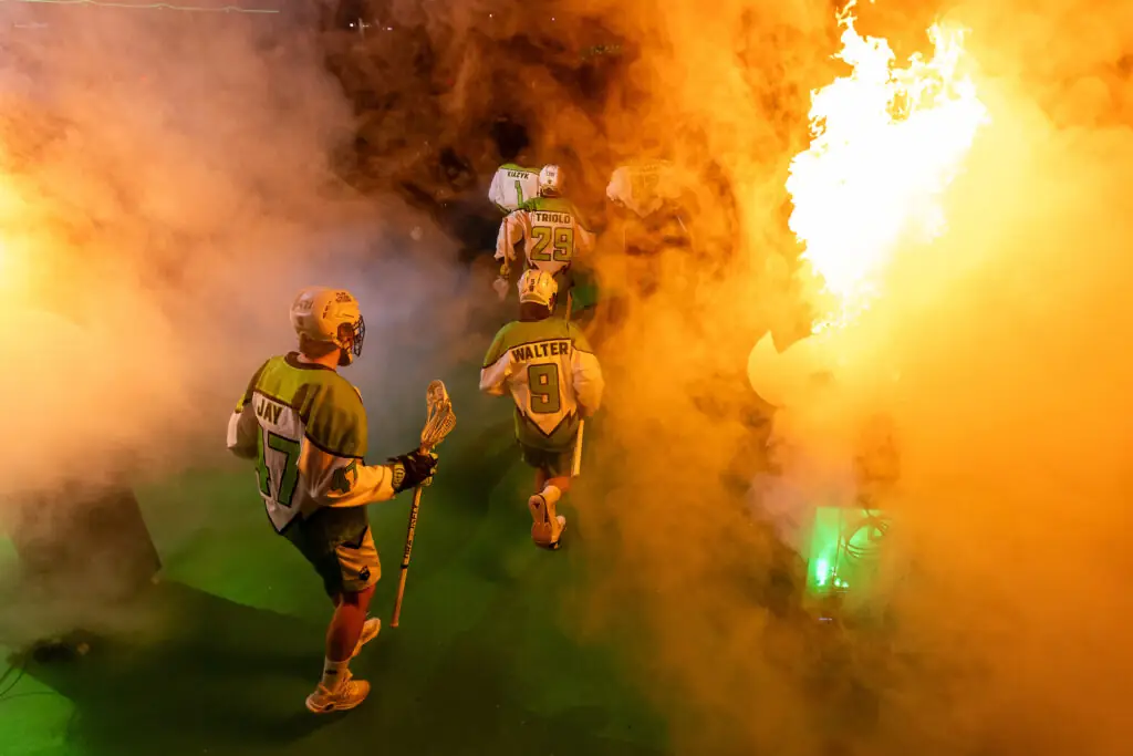 Lacrosse players entering a smoke-filled arena, with flames lighting up the scene.