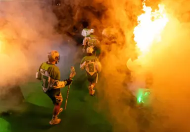 Lacrosse players entering a smoke-filled arena, with flames lighting up the scene.