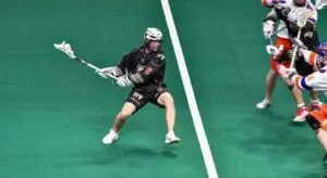 Lacrosse player in black jersey performing a dodge while holding a stick on a green field.