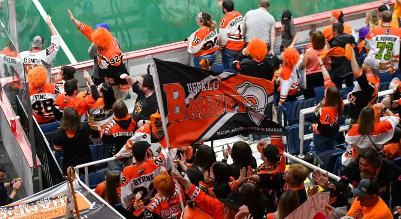 Buffalo Bandits fans cheering and waving a team flag in an indoor arena.