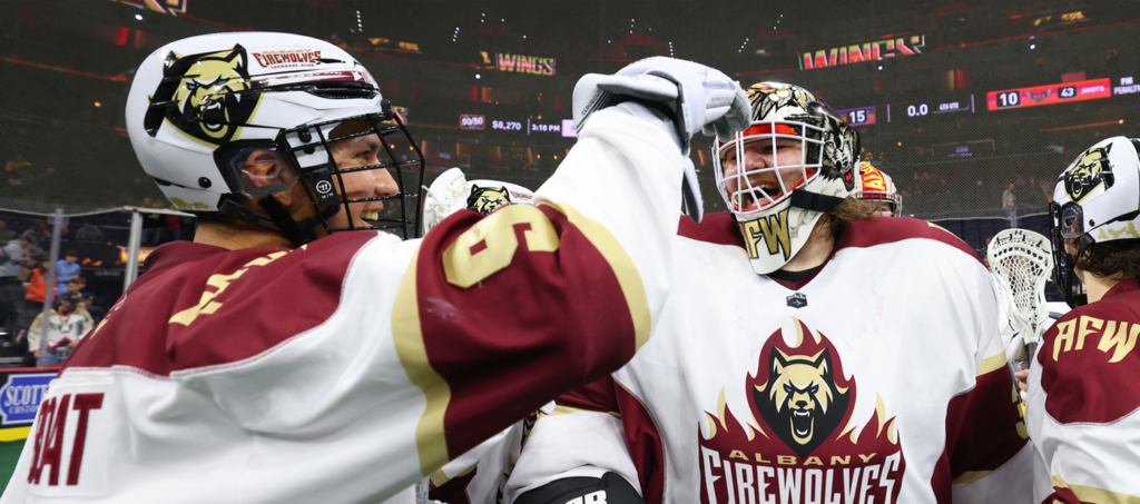 Two Albany Firewolves players celebrate on the field after a game, smiling and interacting.