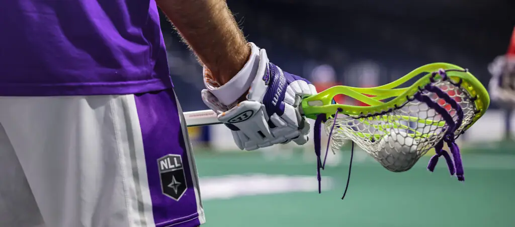 A lacrosse player in a purple jersey holds a stick with a bright green head and ball.