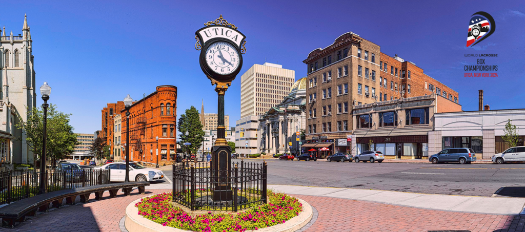 A street view of Utica, New York, featuring a large clock, historic buildings, and colorful flowers along the sidewalk.