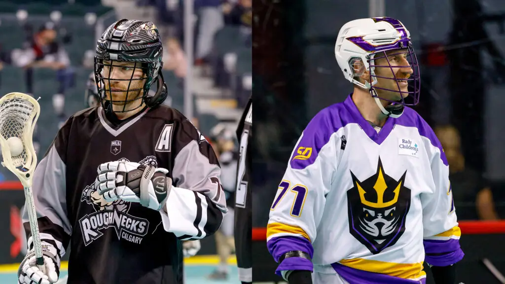 Two lacrosse players face each other on the field, one wearing a black and gray jersey with the "Roughnecks" logo and the letter "A" for captain, while the other wears a white and purple jersey featuring a stylized logo. Both players are equipped with helmets and gloves, holding their sticks.