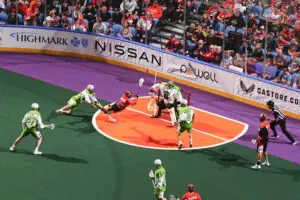Player in red jersey dives to score in lacrosse game, fans cheering
