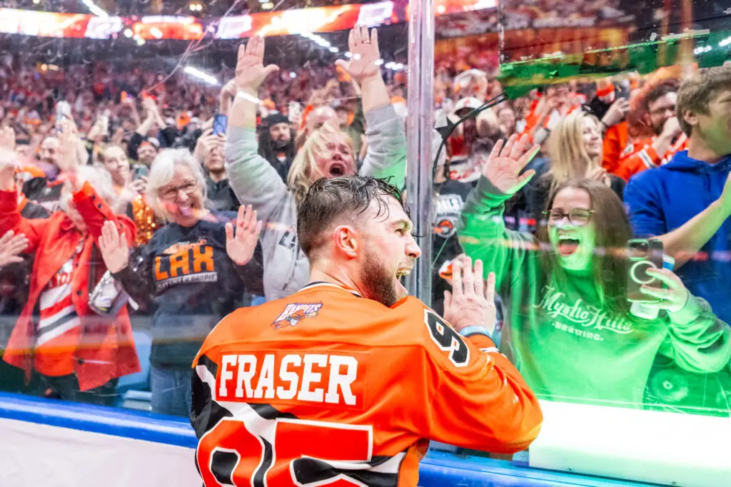 Hockey player Fraser celebrating with cheering fans behind glass barrier