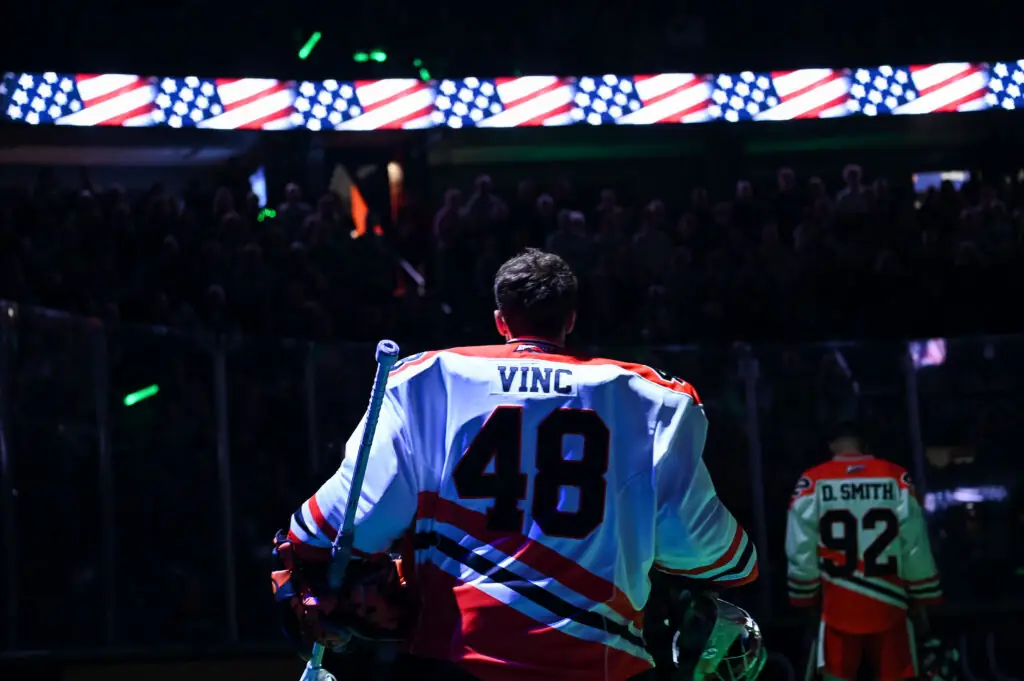 Hockey player Vinc wearing jersey number 48, standing with crowd and American flag in background