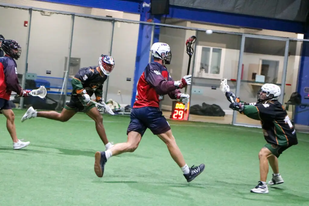Liam Quinn playing indoor lacrosse, jumping while shooting at opposing player in action.