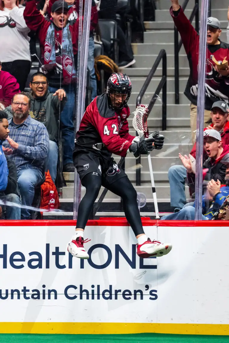 Lacrosse player mid-jump over bench, fans cheering in background, "HealthONE Mountain Children’s" text visible