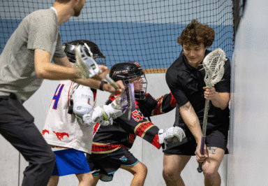 A group of young lacrosse players practice in an indoor facility, focusing on teamwork and skills as they engage in a drill.