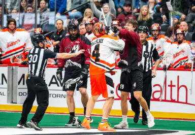 Buffalo Bandits player with "MacKay" jersey in a lacrosse scuffle, referees intervening, spectators watching