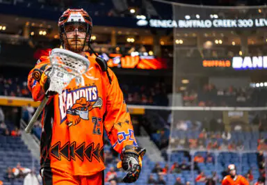 Lacrosse player in orange Buffalo Bandits uniform holds stick on field