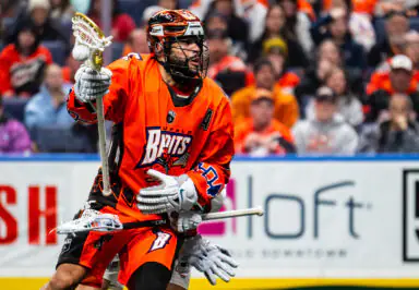 Lacrosse player in action wearing orange Buffalo Bandits jersey, crowd in background
