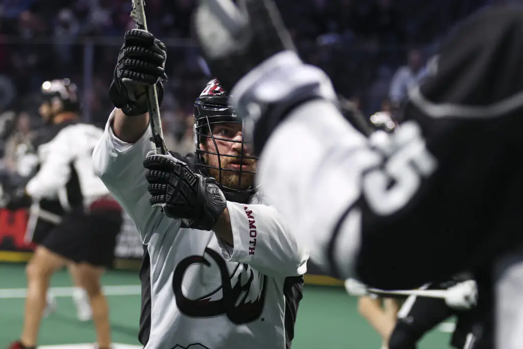 Lacrosse player in white intercepts with raised stick, intense focus