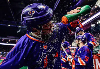 Player in blue lacrosse uniform sprays water on face during game