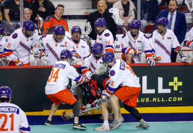 Halifax Thunderbirds lacrosse team on sidelines interacting during a game, with players in action
