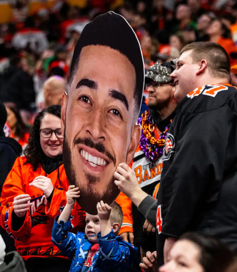 Fans holding a large cutout face, celebrating enthusiastically in sports jerseys