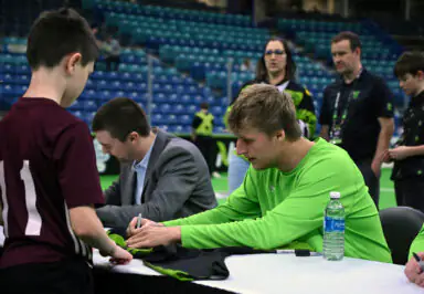Young athlete in green signing an autograph for a fan