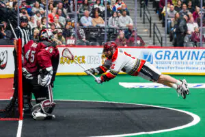 Player diving to score in lacrosse game, goalie blocking